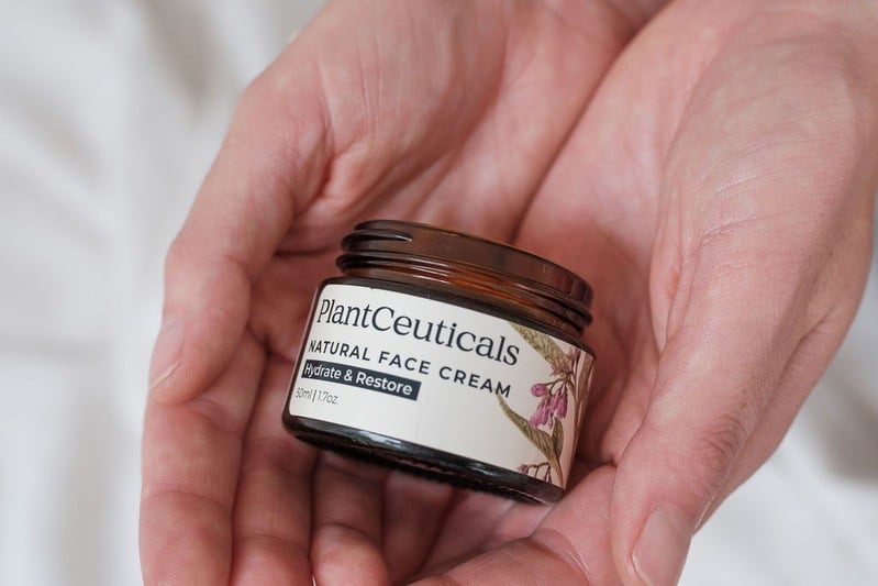 Open jar of PlantCeuticals Natural Face Cream held in cupped hands.